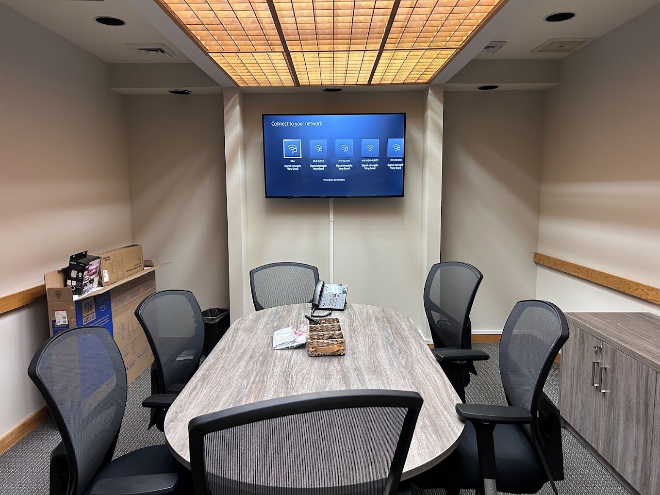 A 55 inch TV mounted on the end wall of a small office meeting room.