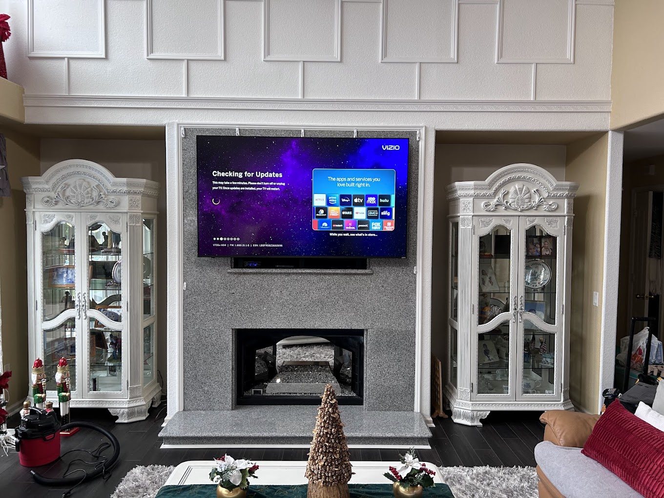 A 65 inch TV mounted above a stone fireplace, centered between two white display cabinets.