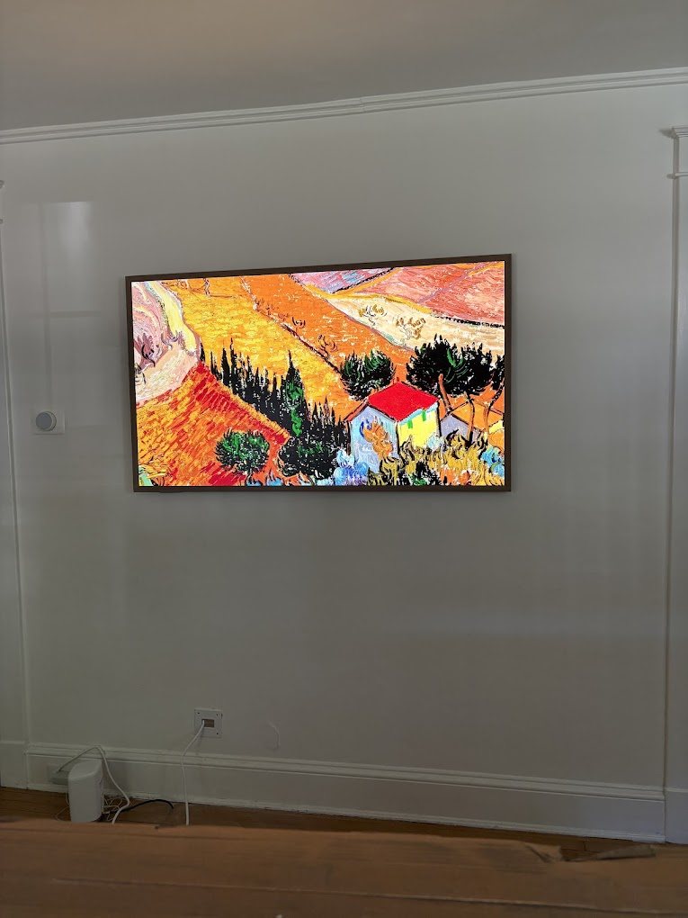 A 55 inch Frame TV hung on a white wall, showing a colorful painting in art mode.
