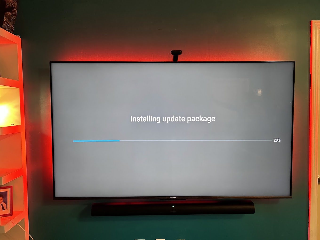 An 85 inch TV mounted on a dark green wall with red LED backlighting and a soundbar mounted below.