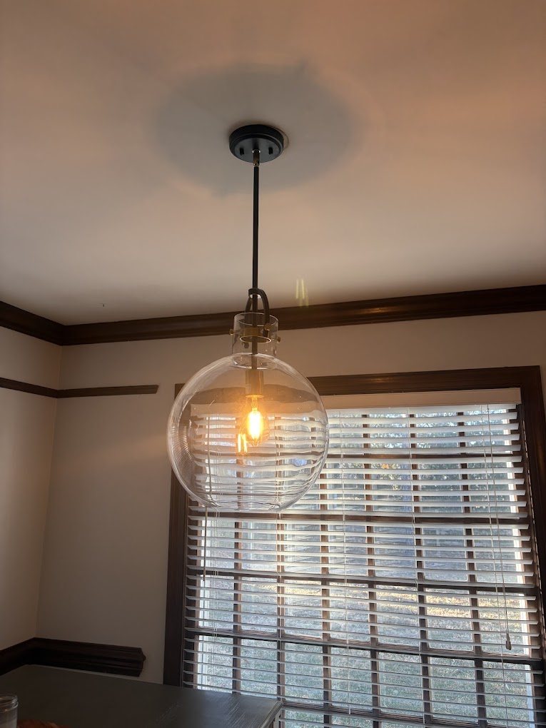 A glass globe pendant light hung in front of a window.